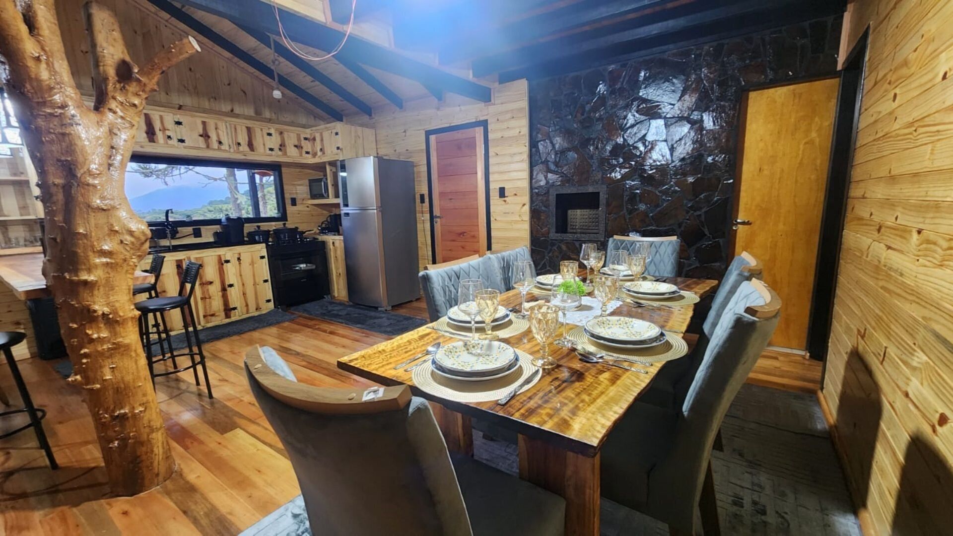 A wooden interior with a dining table set for six, a kitchen area, and a stone wall.