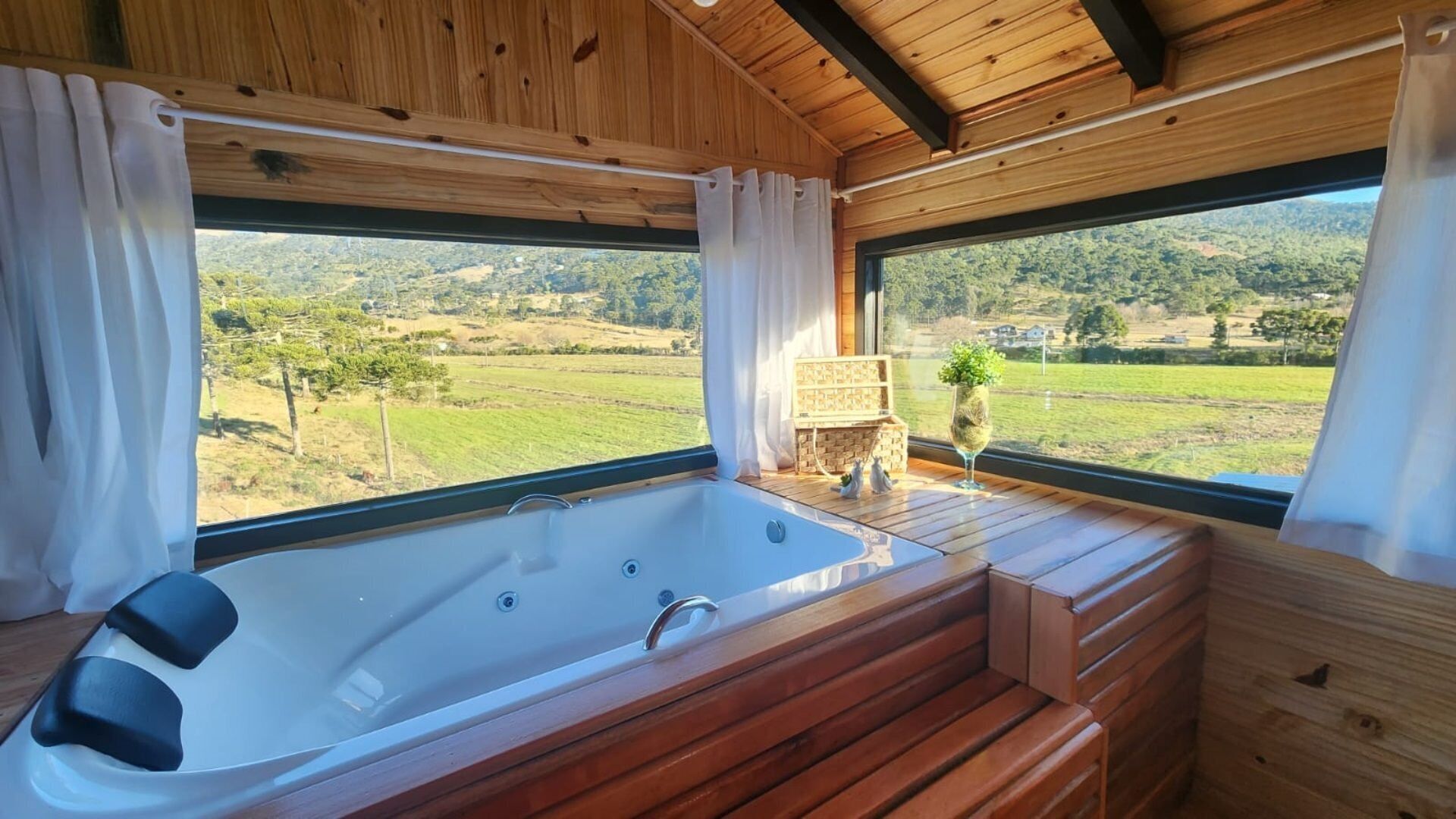 Una baita di legno con una vasca da bagno ampia, panche in legno e vista su un paesaggio verde.