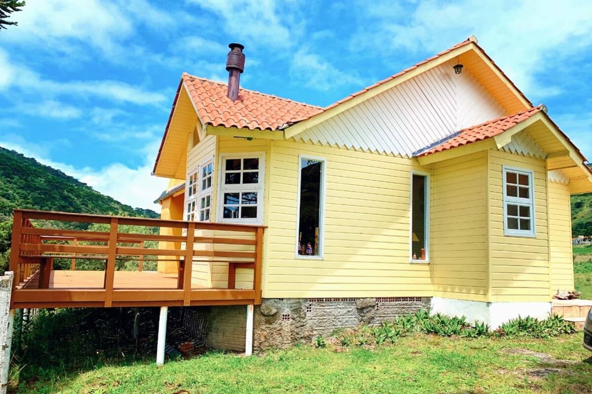 A yellow wooden house with a red-tiled roof, a wooden deck, and a stone foundation.
