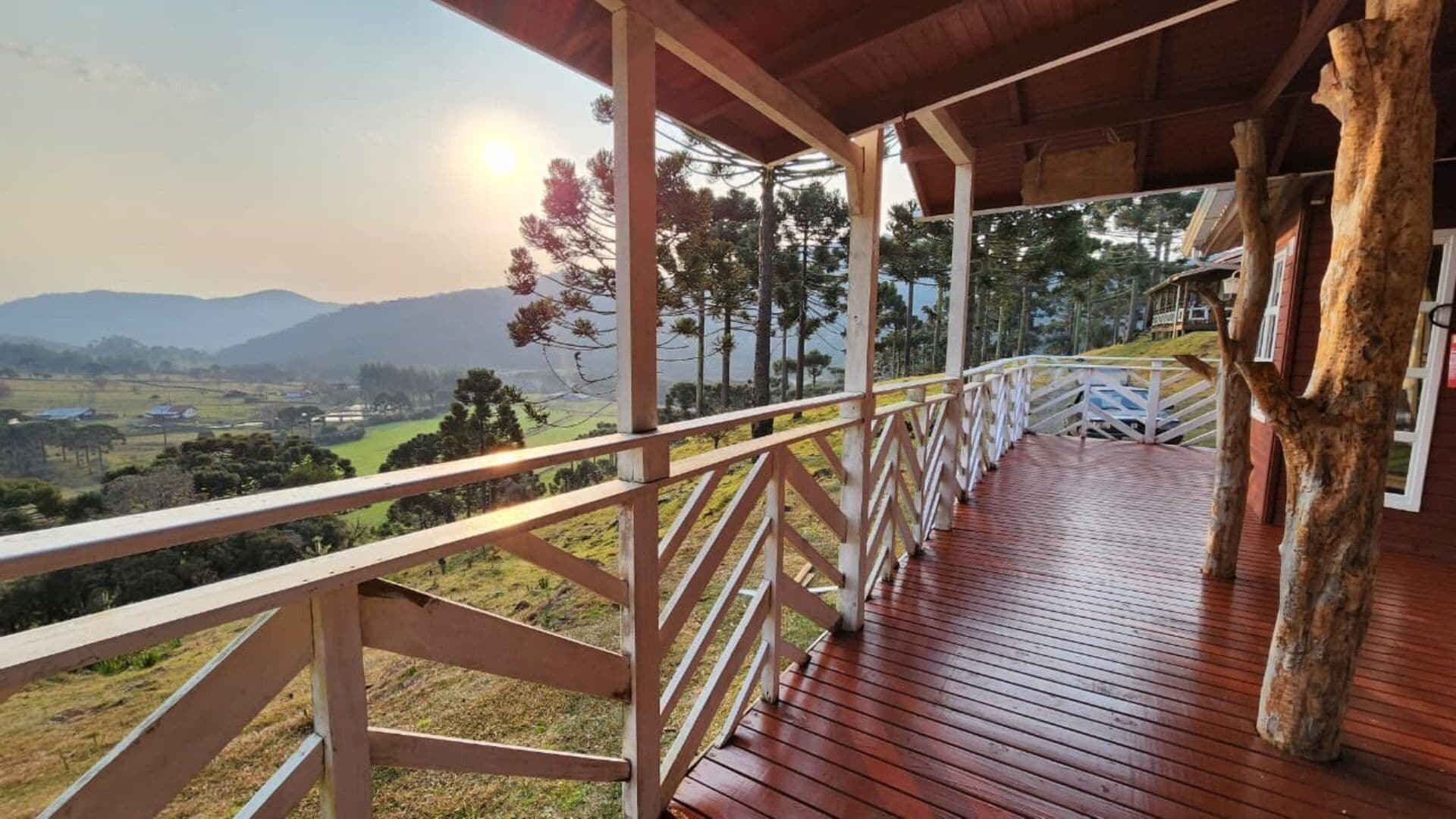 Una terraza de madera con barandilla que da a un paisaje pintoresco con montañas y árboles.