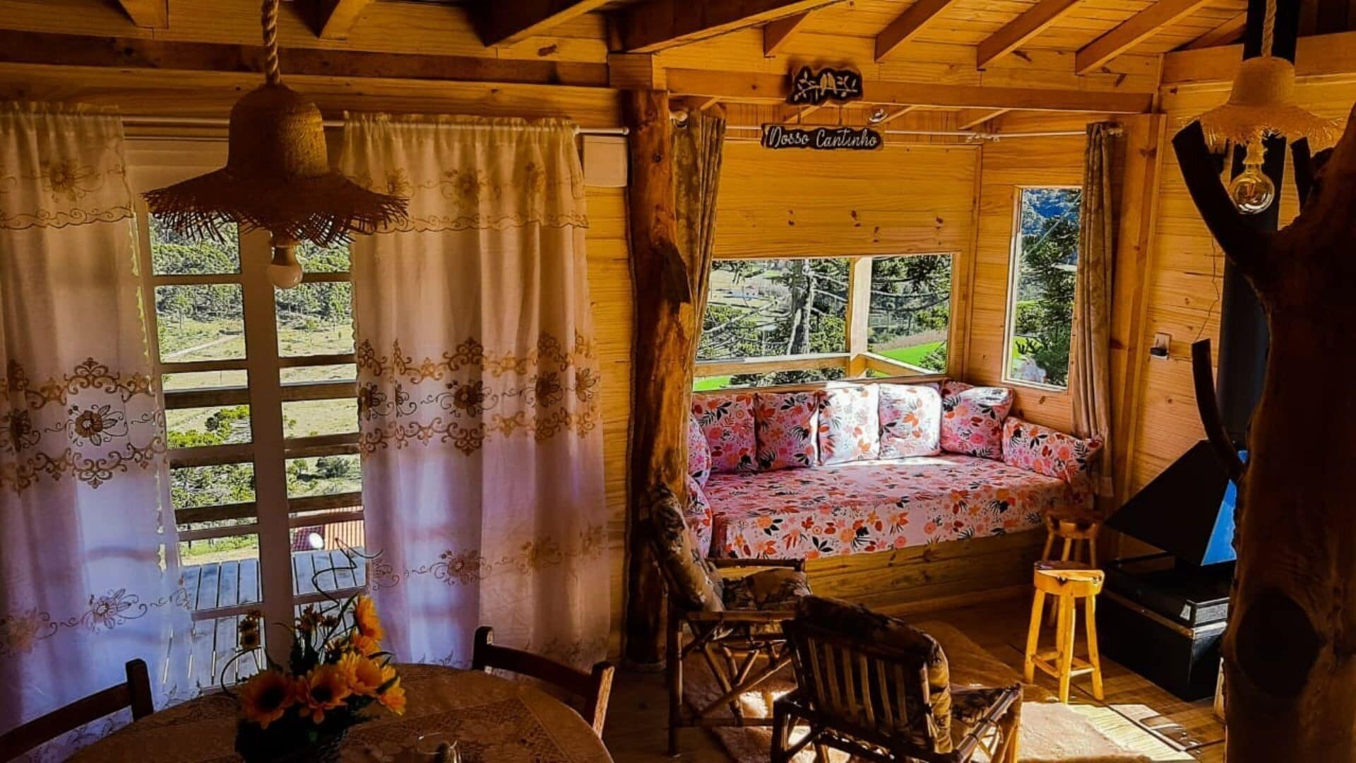 Un acogedor interior de cabaña con techo de madera, una cama con ropa de cama floral, una mesa de comedor con un jarrón de girasoles y un letrero que dice 