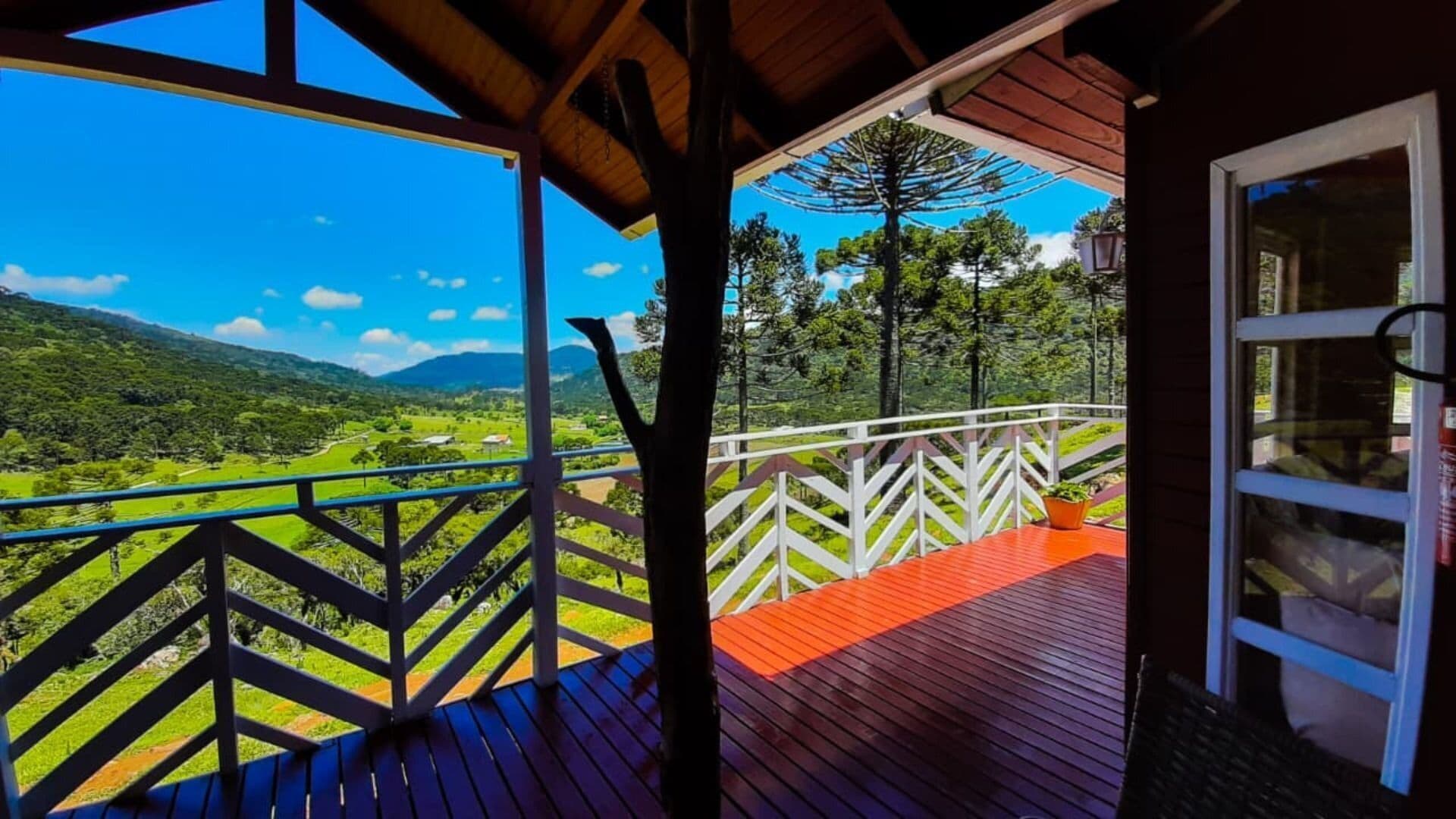 Une terrasse en bois dotée d’une balustrade, qui offre une vue sur un paysage verdoyant et des montagnes.