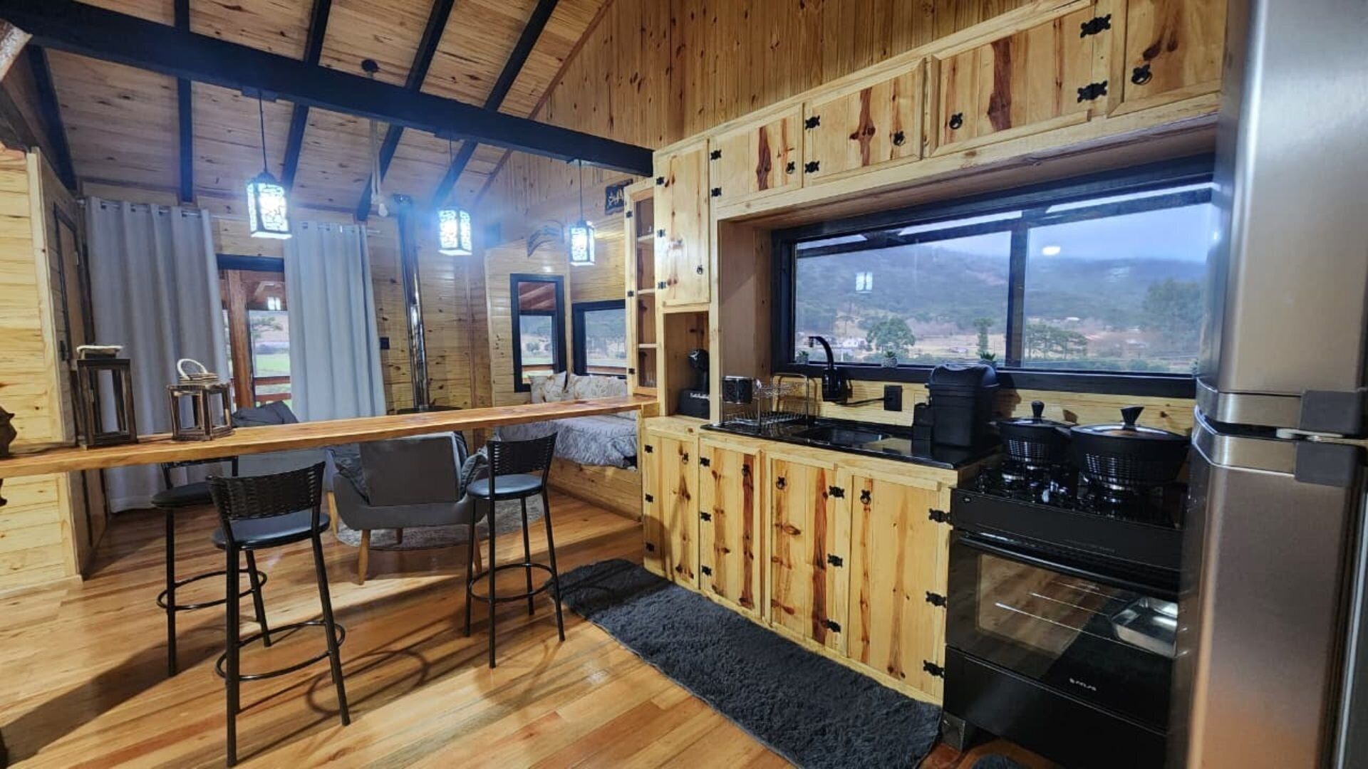 Cocina compacta con alacenas de madera, una barra y un ventanal con vistas amplias.