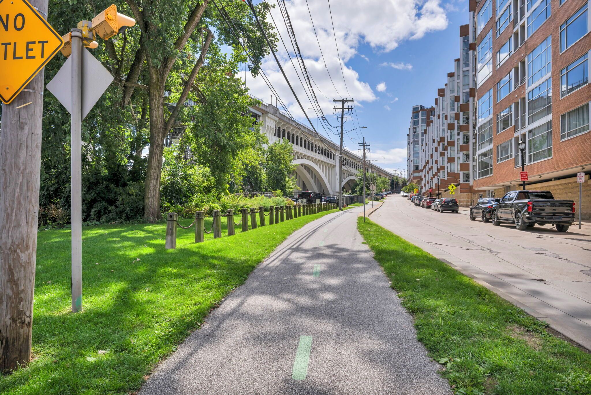 A pathway with a 'NO TROLLEY' sign, lined with trees and a building with arched windows in the background.