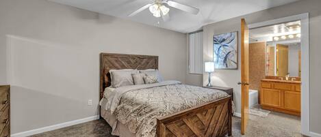 A bedroom with a wooden bed, a ceiling fan, a nightstand, a mirror, and a bathroom with a vanity and sink.