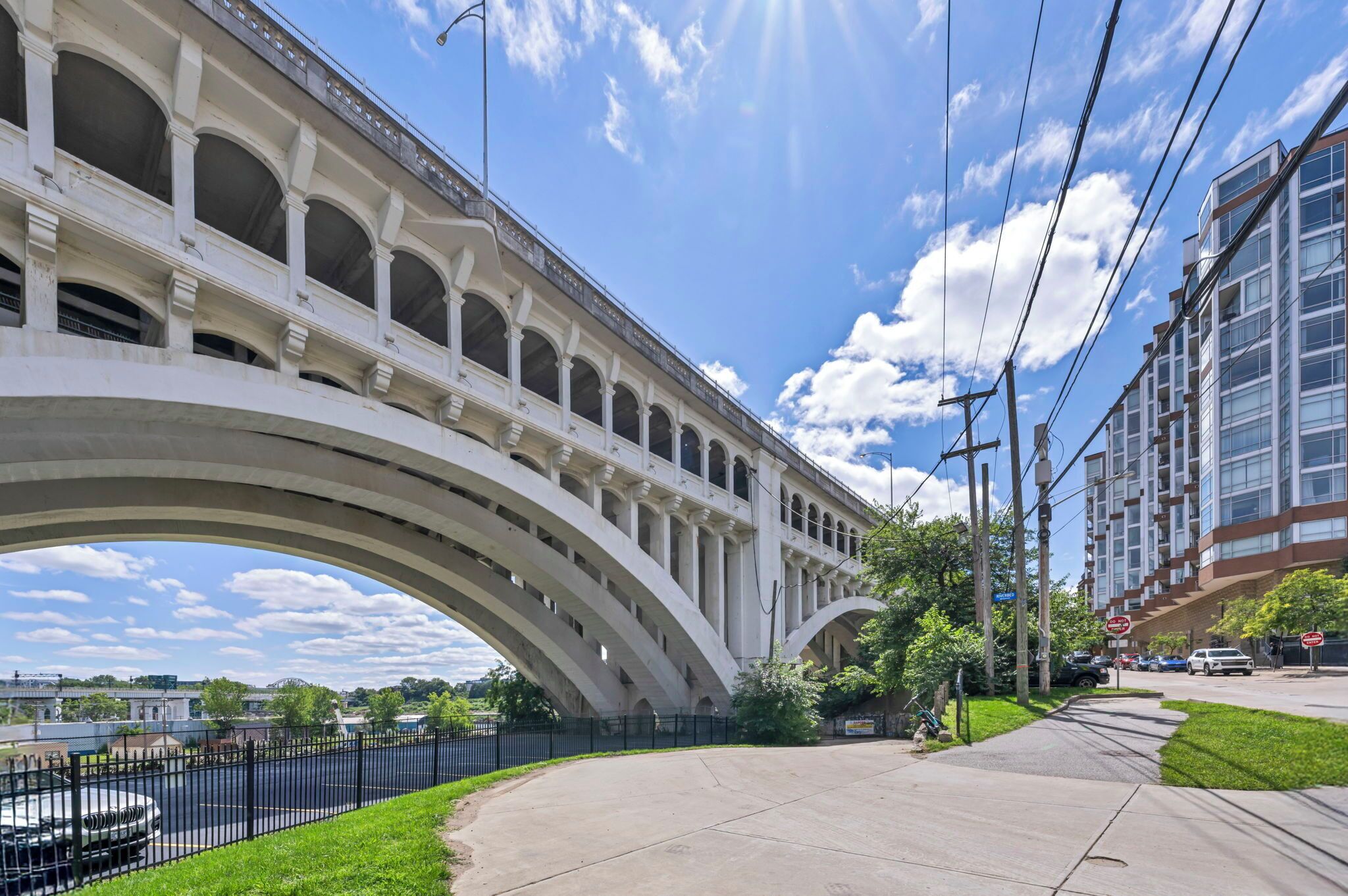 A large white arched bridge over a road, with a modern building on the right and a clear blue sky.