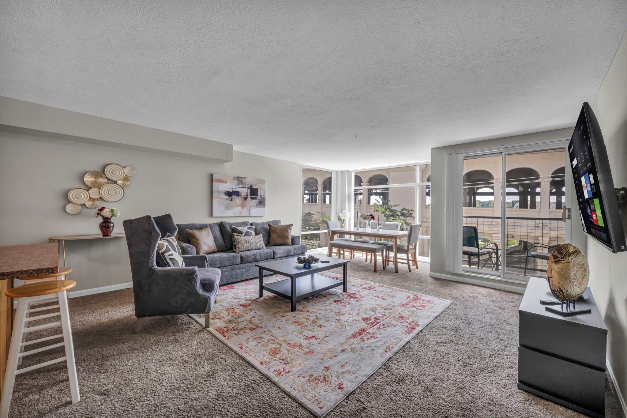 A spacious living room with a gray sofa, a coffee table, and a large window offering a view of an outdoor patio.