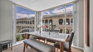 Un coin repas avec une table et des chaises en verre, de grandes fenêtres offrant une vue sur un pont en arc et des bâtiments.