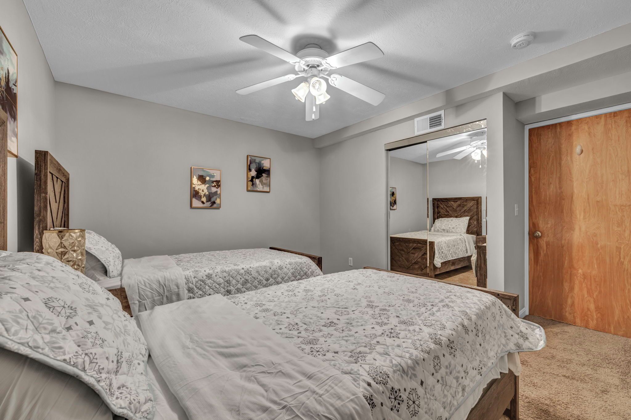 A bedroom with two beds, a ceiling fan, a wooden door, and a large mirror on the wall.