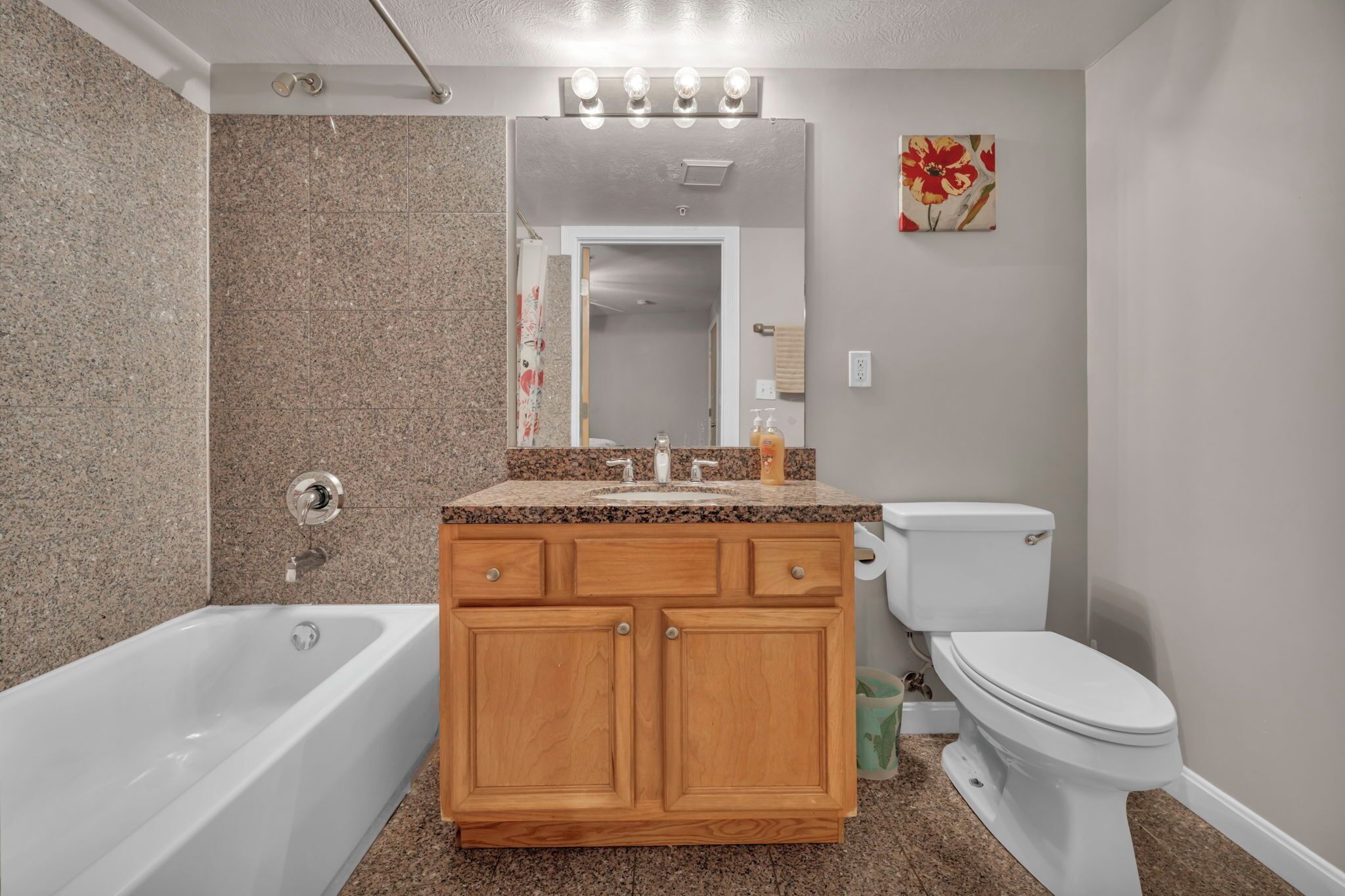 Une salle de bain avec un lavabo sur un plan de travail en granit, des meubles en bois, des toilettes blanches et une baignoire.