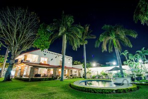 Un hôtel bien éclairé, doté d’une piscine, de palmiers et d’un vaste espace extérieur aménagé pour se détendre.