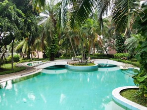 A pool with a curved design, surrounded by lush greenery and palm trees. - Best Deal 2Br Apartment At Taman Beverly (Surabaya)