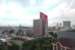A modern building with a unique red structural element, surrounded by a cityscape with various buildings and greenery. - Best Deal 2Br Apartment At Taman Beverly (Surabaya)