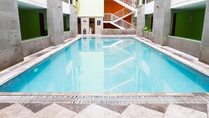 Ein Schwimmbecken mit gefliestem Deck, umgeben von Mauern mit grünen und weißen Paneelen, und einer Treppe, die zu einer oberen Ebene führt.
