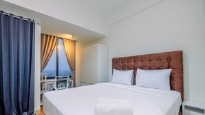 A hotel room with a large bed, a view of the city, and a balcony with a table and chairs. - Comfy And Nice Studio At Lrt City Bekasi Apartment (Bekasi)