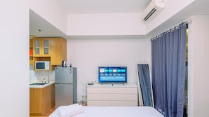 A compact hotel room with a bed, a small kitchenette, a flat-screen TV, and a window with curtains. - Comfy And Nice Studio At Lrt City Bekasi Apartment (Bekasi)