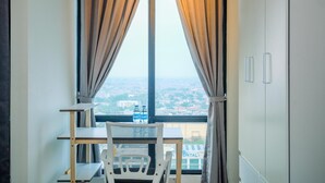 A room with a large window, a chair, a small table, and a wardrobe. - Comfy And Nice Studio At Lrt City Bekasi Apartment (Bekasi)