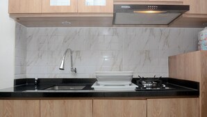 A kitchen with wooden cabinets, a black countertop, a sink, a stove, and a backsplash with white tiles. - Neat Studio At Lrt City Bekasi Apartment (Bekasi)
