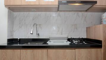 Uma cozinha com armários de madeira, bancada preta, pia, fogão e painel de azulejos brancos.