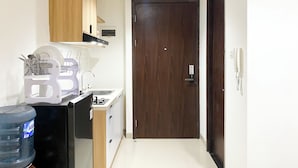 A compact kitchen with wooden cabinets, a built-in sink, and a water dispenser. - Simple Studio At Lrt City Bekasi Apartment By Travelio (Bekasi)