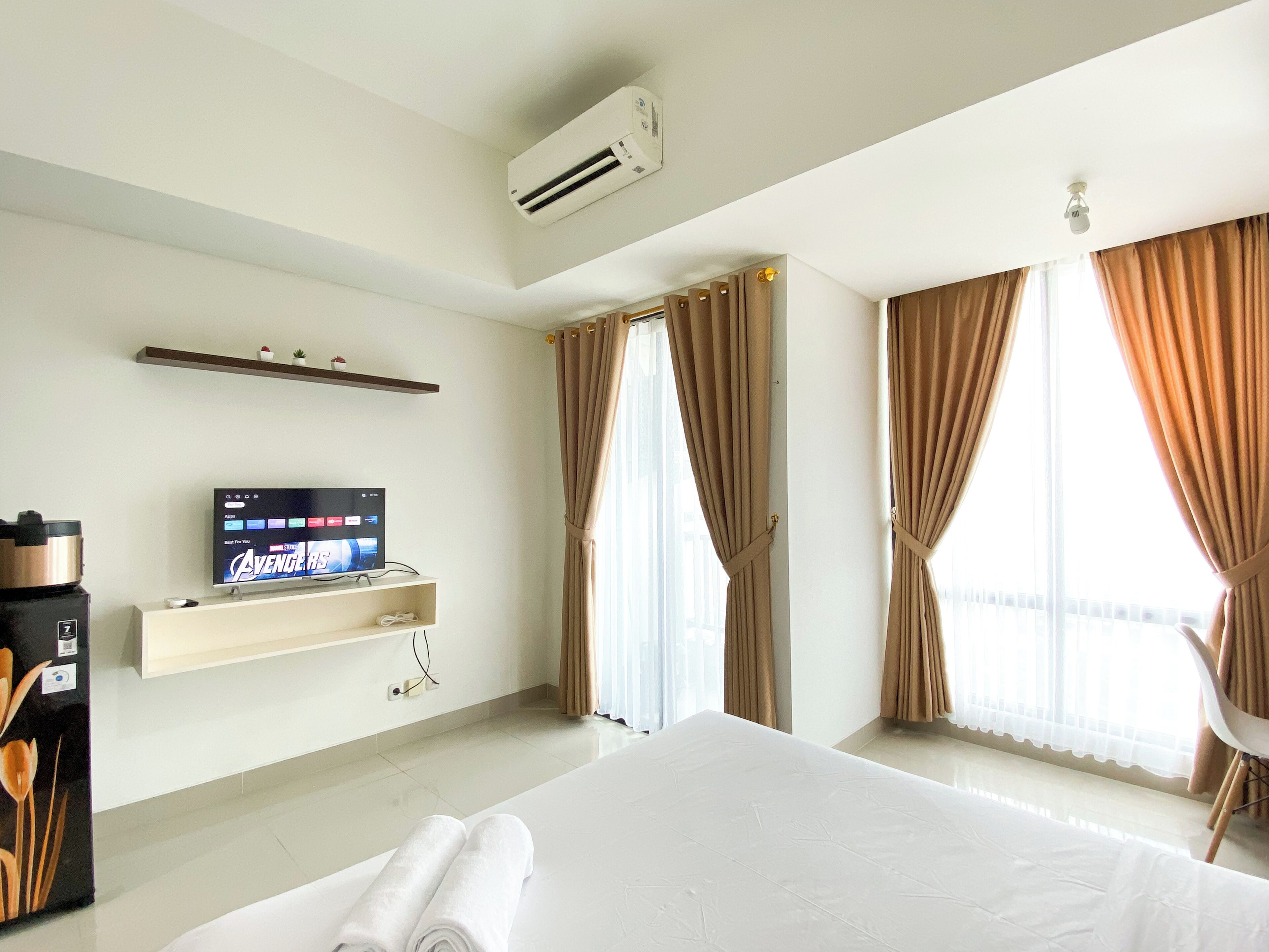 A hotel room with a bed, a TV on a stand, an air conditioning unit, a window with curtains, and a chair.