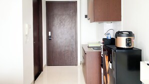 A compact kitchen with a dark wooden door, a black refrigerator, and a rice cooker on the counter. - Homey And Nice Studio At Lrt City Bekasi Apartment (Bekasi)