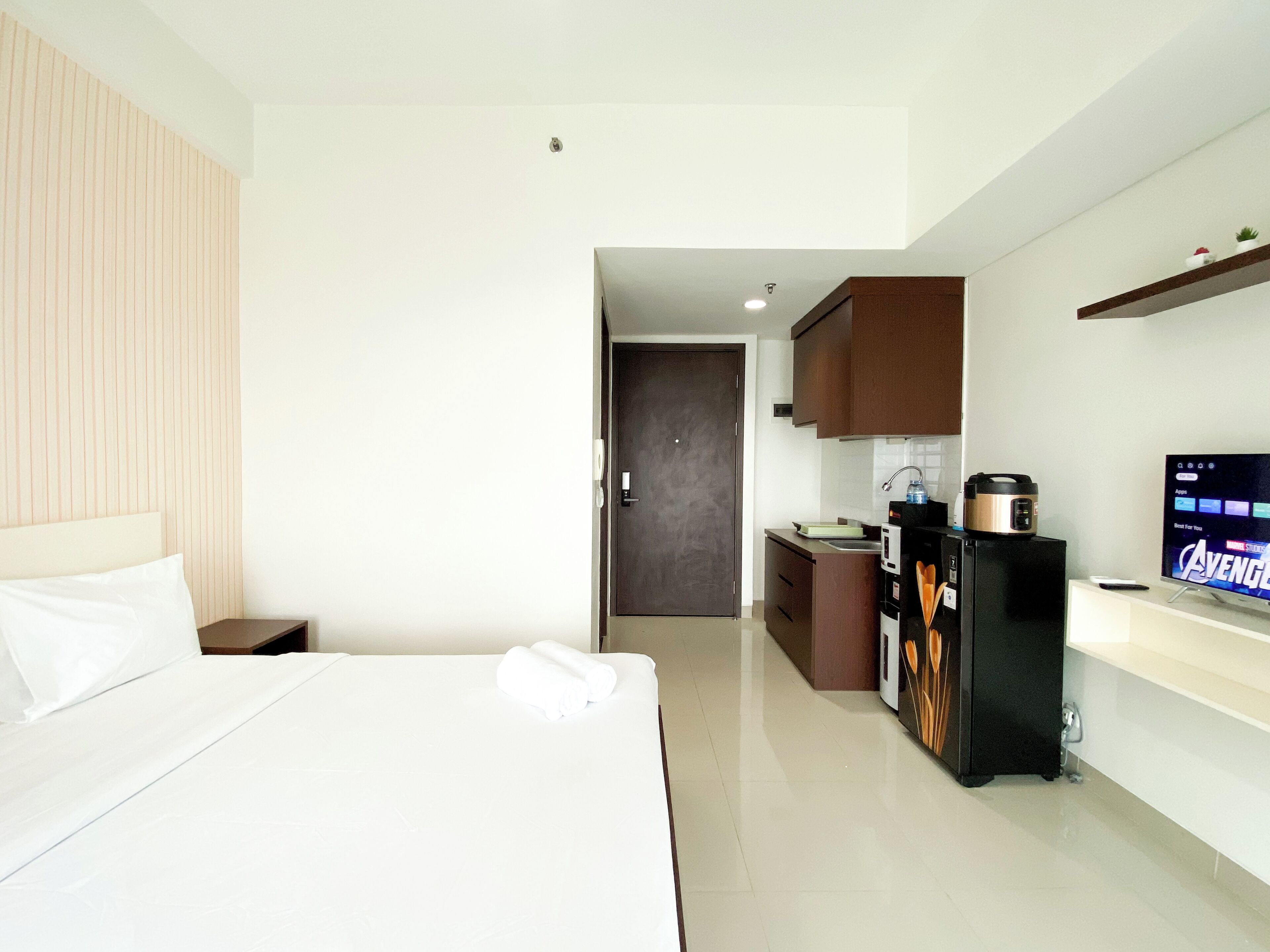 A hotel room with a bed, a small kitchenette, a television, and a refrigerator.