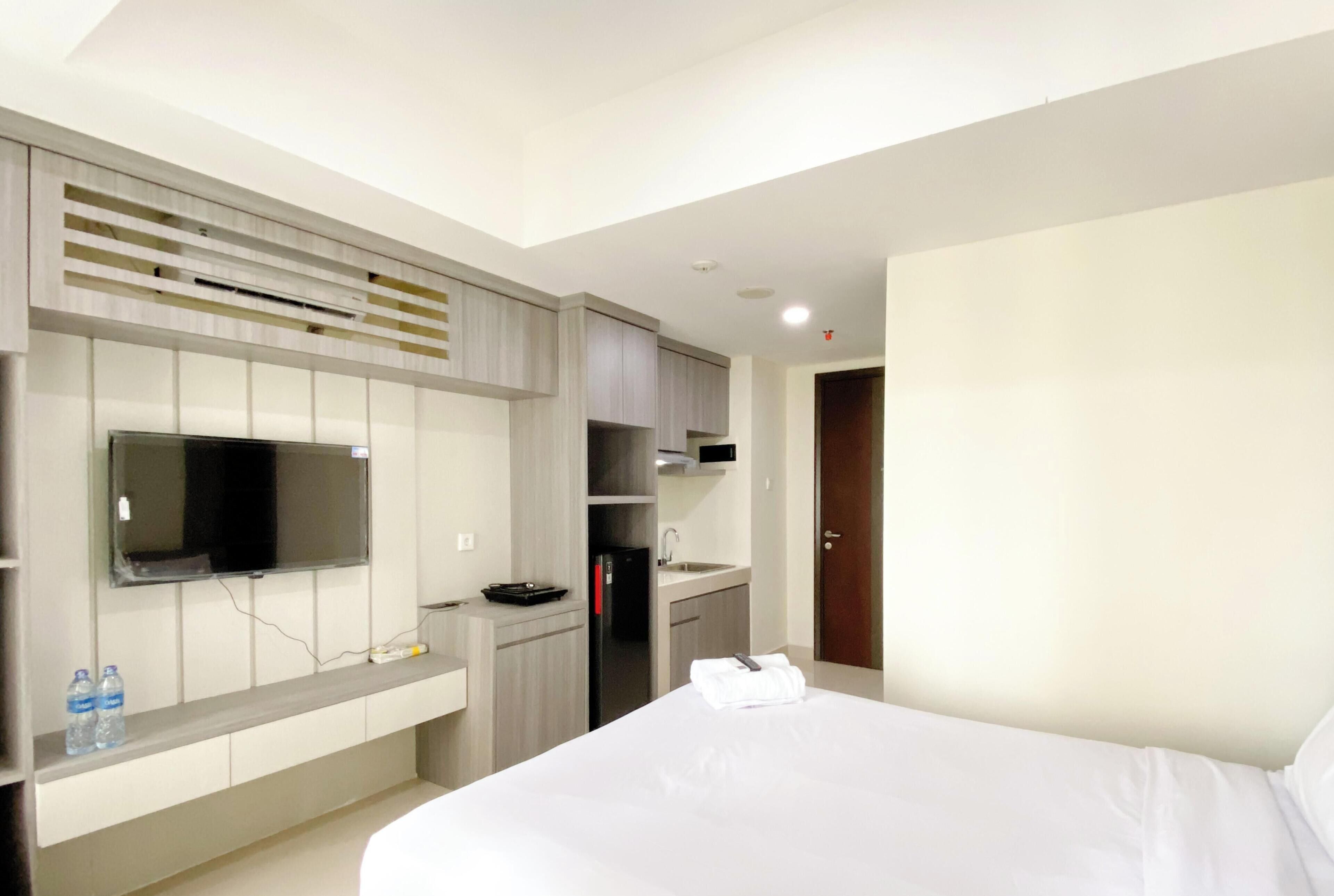 Une chambre d’hôtel moderne dotée d’un grand lit, d’un téléviseur à écran plat fixé au mur, d’un coin cuisine intégré et d’une porte donnant accès à la salle de bain.