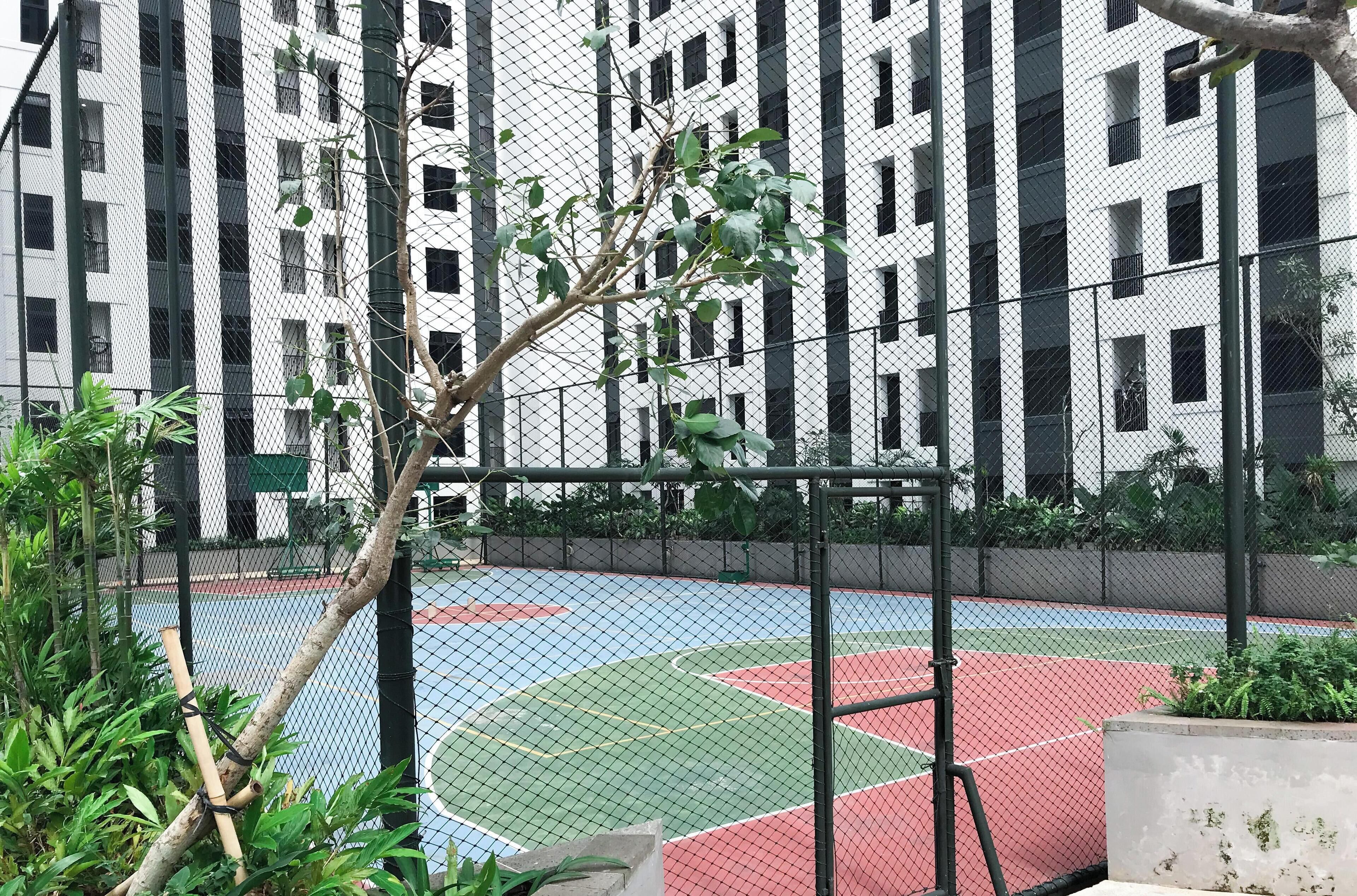 Un terrain de basket entouré d’une clôture en treillis métallique, avec un bâtiment en arrière-plan.