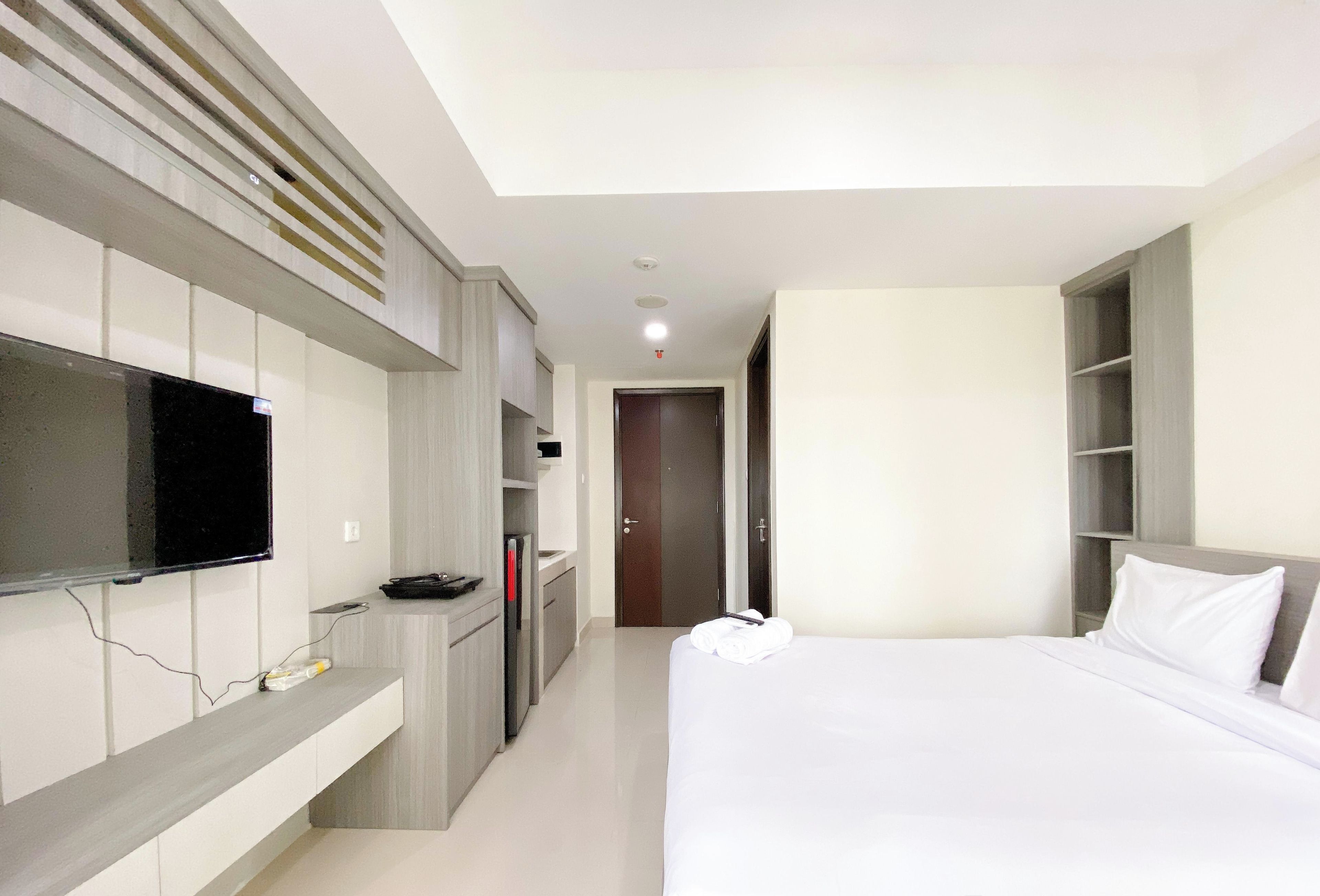 A hotel room with a bed, a TV mounted on the wall, a desk with a chair, and a wardrobe.