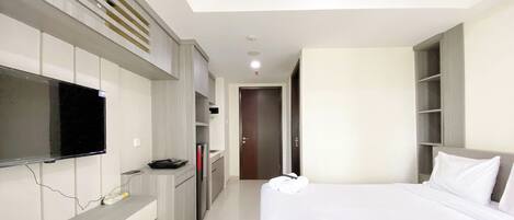 A hotel room with a bed, a TV mounted on the wall, a desk with a chair, and a wardrobe.