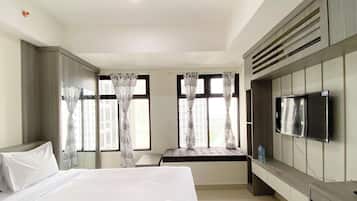 Quarto de hotel com cama grande, televisão fixada na parede e janela com cortinas.