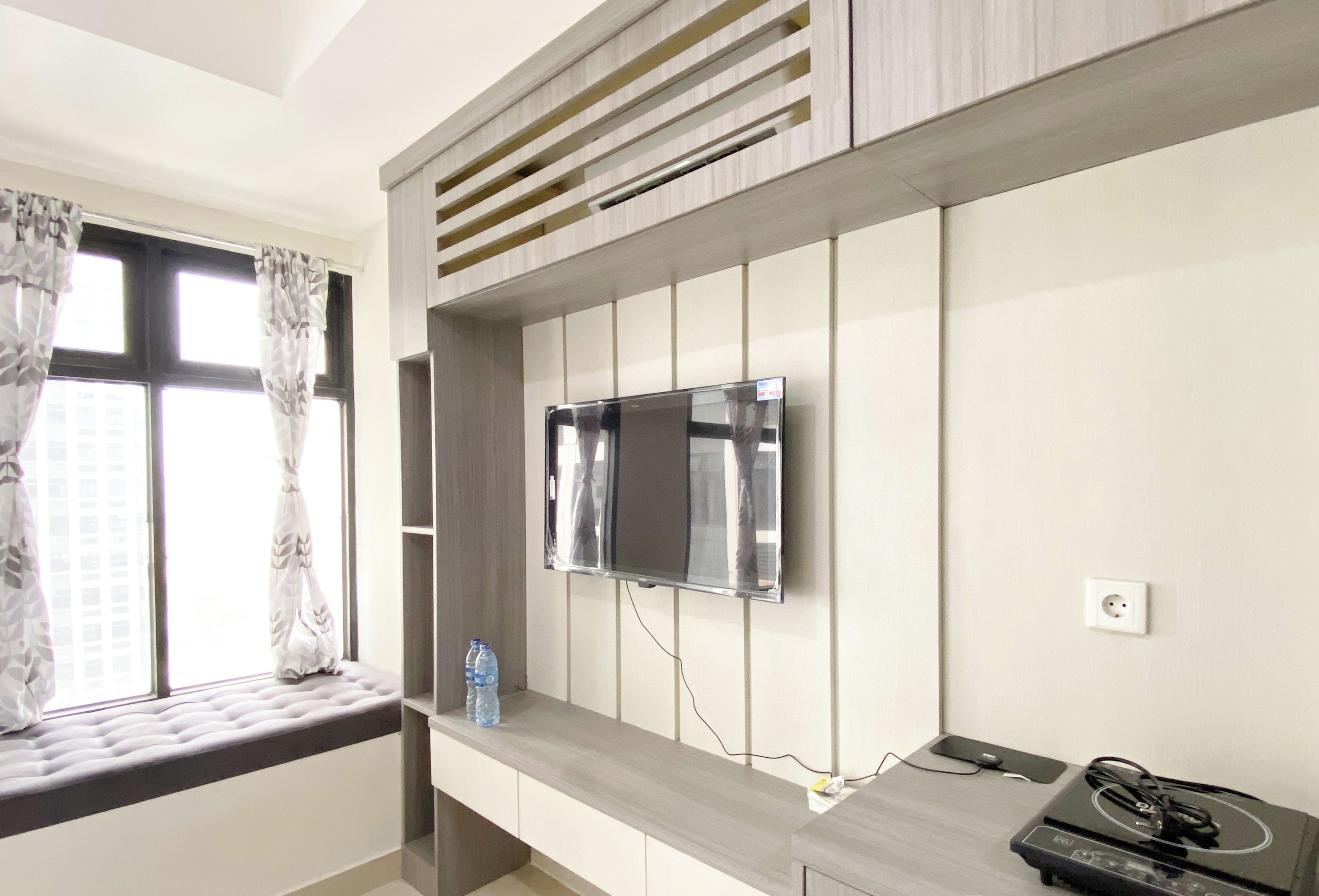 Habitación de hotel moderna con un ventanal grande, un televisor de pantalla plana montado en la pared, una botella de agua en el alféizar y un calentador portátil en el escritorio.