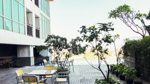 An outdoor patio with tables and chairs, surrounded by potted plants and a view of a building. - Scenic Modern Studio Room At Tamansari Papilio Apartment (Surabaya)