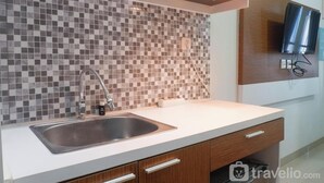 A modern kitchen with a tiled backsplash, stainless steel sink, wooden cabinets, and a built-in microwave. - Scenic Modern Studio Room At Tamansari Papilio Apartment (Surabaya)