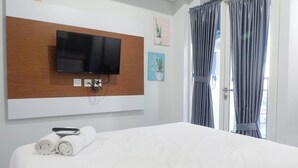 A hotel room with a large bed, a flat-screen TV mounted on a wooden panel, and a window with curtains. - Scenic Modern Studio Room At Tamansari Papilio Apartment (Surabaya)