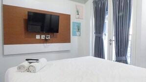 A hotel room with a large bed, a flat-screen TV mounted on a wooden panel, and a window with curtains. - Scenic Modern Studio Room At Tamansari Papilio Apartment (Surabaya)