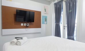 A hotel room with a large bed, a flat-screen TV mounted on a wooden panel, and a window with curtains. - Scenic Modern Studio Room At Tamansari Papilio Apartment (Surabaya)