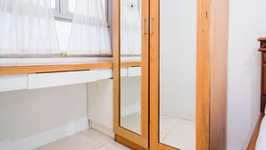 A room with a wooden wardrobe, a window with sheer curtains, and a white wall. - Simply Studio Room At Titanium Square Apartment (Jakarta)