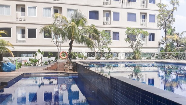 A swimming pool with tiled walls, surrounded by a fence and palm trees. - Simply Studio Room At Titanium Square Apartment (Jakarta)