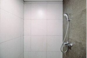 A shower with a handheld showerhead and a wall-mounted faucet in a tiled bathroom. - Homey And Restful Studio Lrt City Bekasi Apartment (Bekasi)