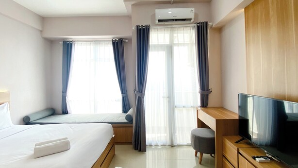 A modern hotel room with a bed, a desk, a television, and an air conditioning unit. - Wonderful And Homey Studio Vasanta Innopark Apartment (Cikarang)