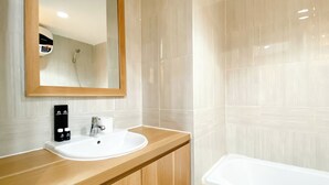 A modern bathroom with a wooden vanity, a white sink, a mirror, and a bathtub. - Wonderful And Homey Studio Vasanta Innopark Apartment (Cikarang)