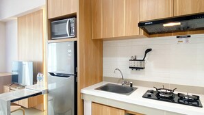 A modern kitchen with wooden cabinets, a stainless steel refrigerator, a microwave, a sink, and a gas stove. - Wonderful And Homey Studio Vasanta Innopark Apartment (Cikarang)