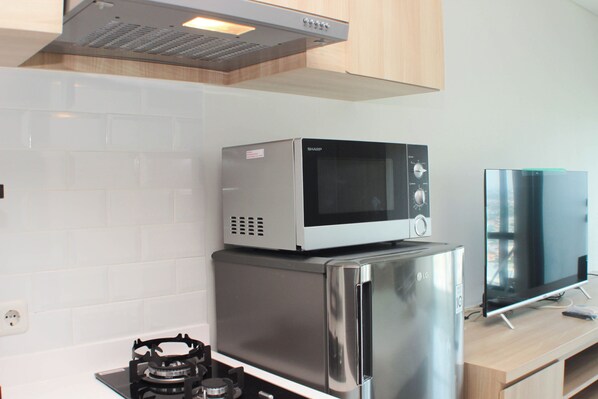 A kitchen with a gas stove, a microwave, a refrigerator, and a flat-screen TV.