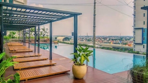 A rooftop pool area with wooden loungers and a potted plant. - Wooden Style Studio At Lrt City Bekasi Apartment (Bekasi)
