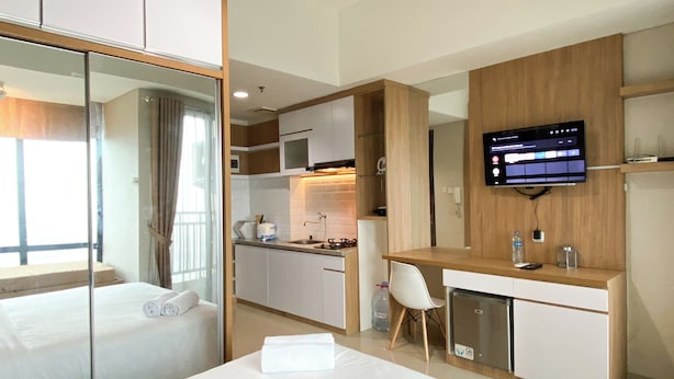 A hotel room with a bed, a desk, a television, and a kitchenette. - Wooden Style Studio At Lrt City Bekasi Apartment (Bekasi)