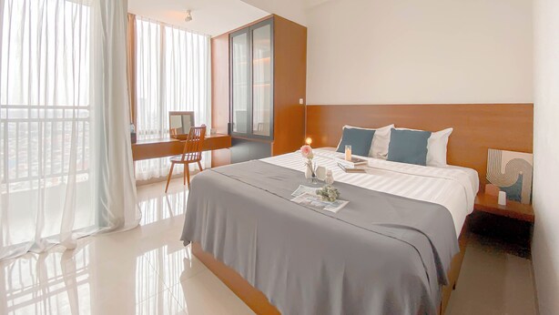 A hotel room with a large bed, a desk, and a window with sheer curtains. - Strategic And Homey Studio At Lrt City Bekasi Apartment (Bekasi)