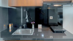 A modern kitchen with a stainless steel sink, a built-in stove, and wooden cabinets. - Strategic And Homey Studio At Lrt City Bekasi Apartment (Bekasi)