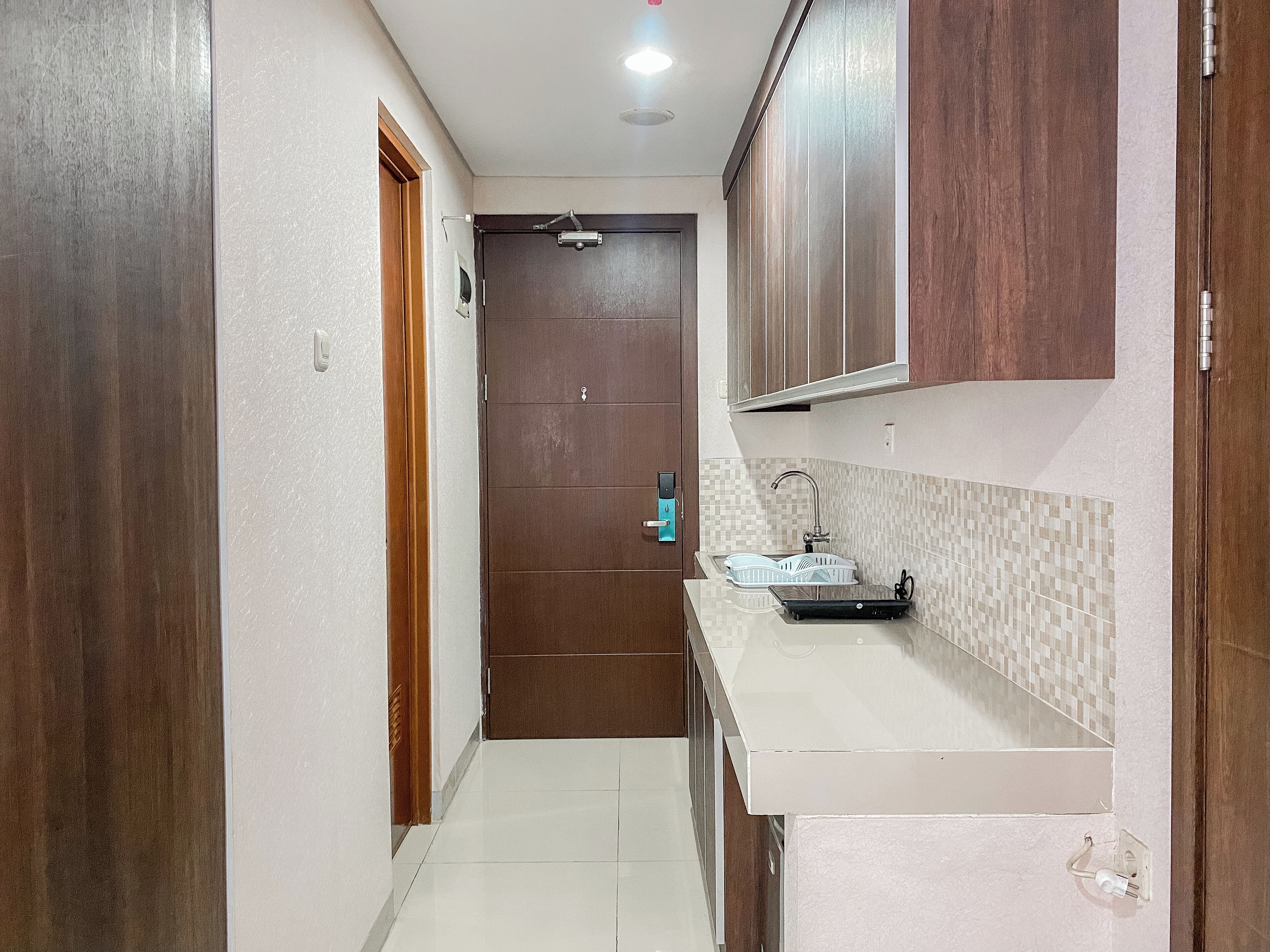 A narrow hallway leading to a kitchen with wooden cabinets, a countertop, and a tiled backsplash.